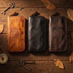 Three vintage leather long zip wallets in mustard tan, black and dark brown on wooden table with antique keys