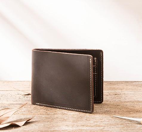 Brown distressed full-grain leather billfold wallet on wooden table with leaves