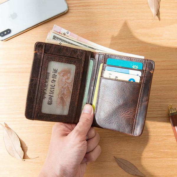 Open dark brown leather billfold wallet with ID window, cards and cash, held in hand