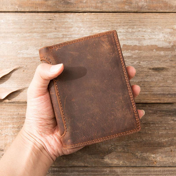 Hand holding brown distressed full-grain leather billfold wallet, front view