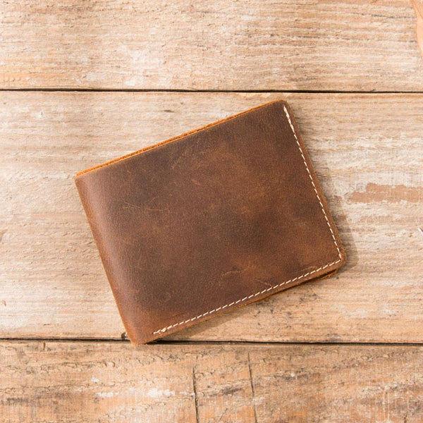 Brown distressed full-grain leather billfold wallet on wooden table with leaves